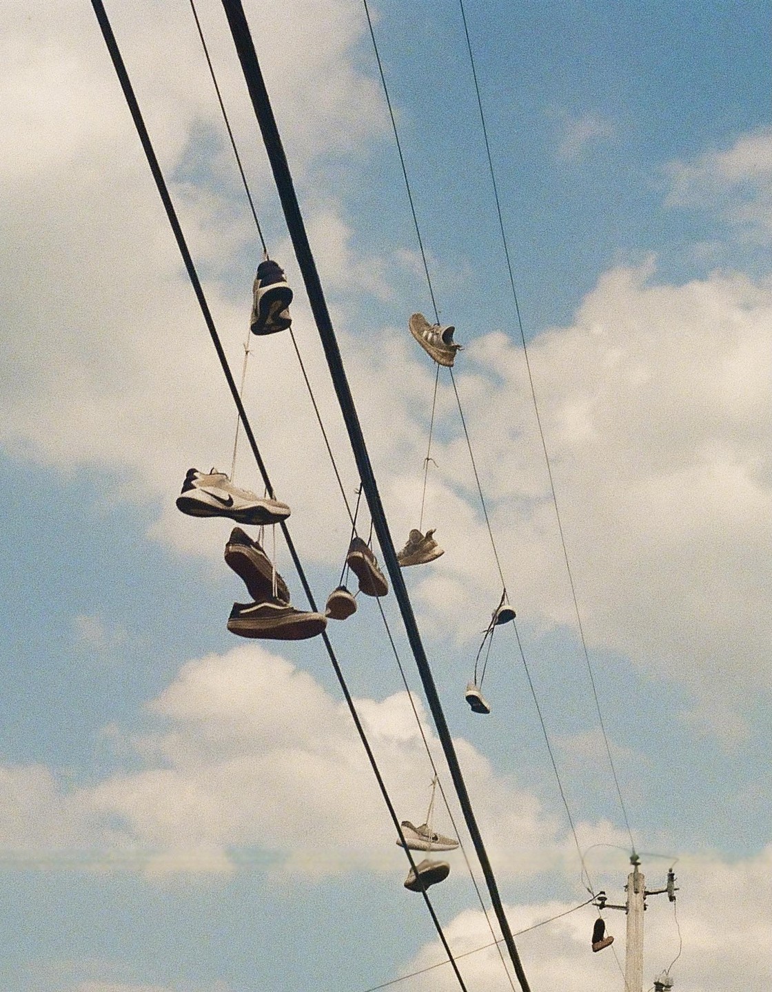 Many pairs of shoes hang from power lines against a cloudy sky.