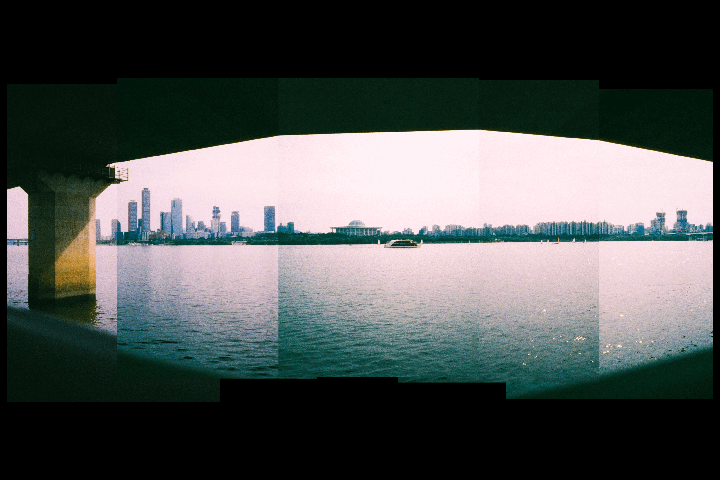 A panoramic view of a city skyline across a body of water, seen from under a bridge.