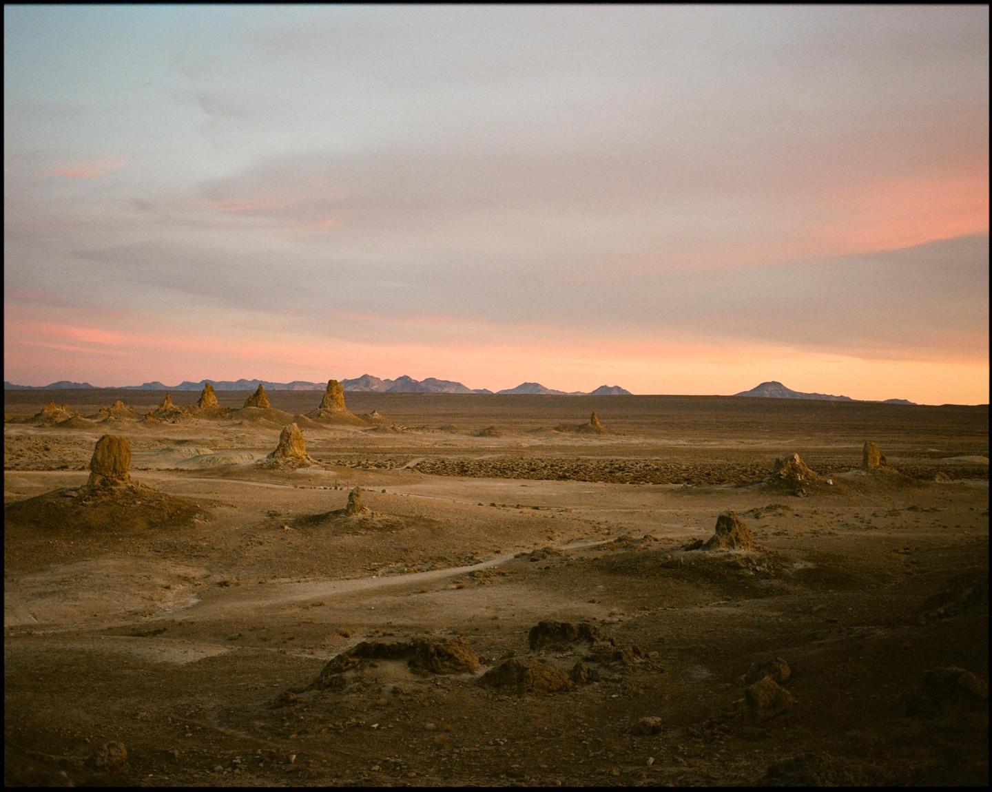 A desert landscape with tufa formations is visible under a colorful sunset sky.