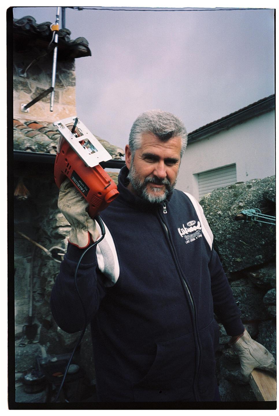 A man with a beard and gray hair holds a jigsaw in his gloved hand.