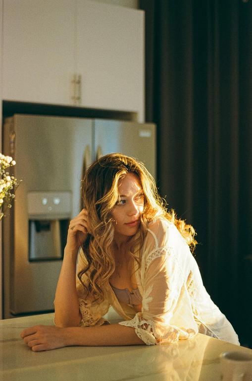 A woman with long, curly hair leans on a counter in a kitchen, illuminated by golden hour sunlight.