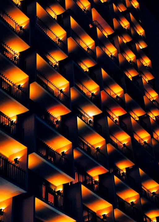 A building facade with many balconies is illuminated by warm orange lights at night.