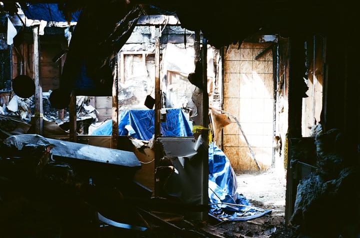 Sunlight streams into a destroyed room with blue tarps covering parts of the floor and walls.