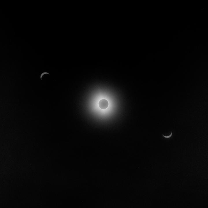 A total solar eclipse is visible in the dark sky, flanked by two crescent shapes.