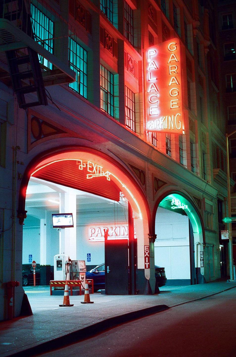 A neon sign for Palace Garage Parking illuminates the entrance to a parking garage at night.