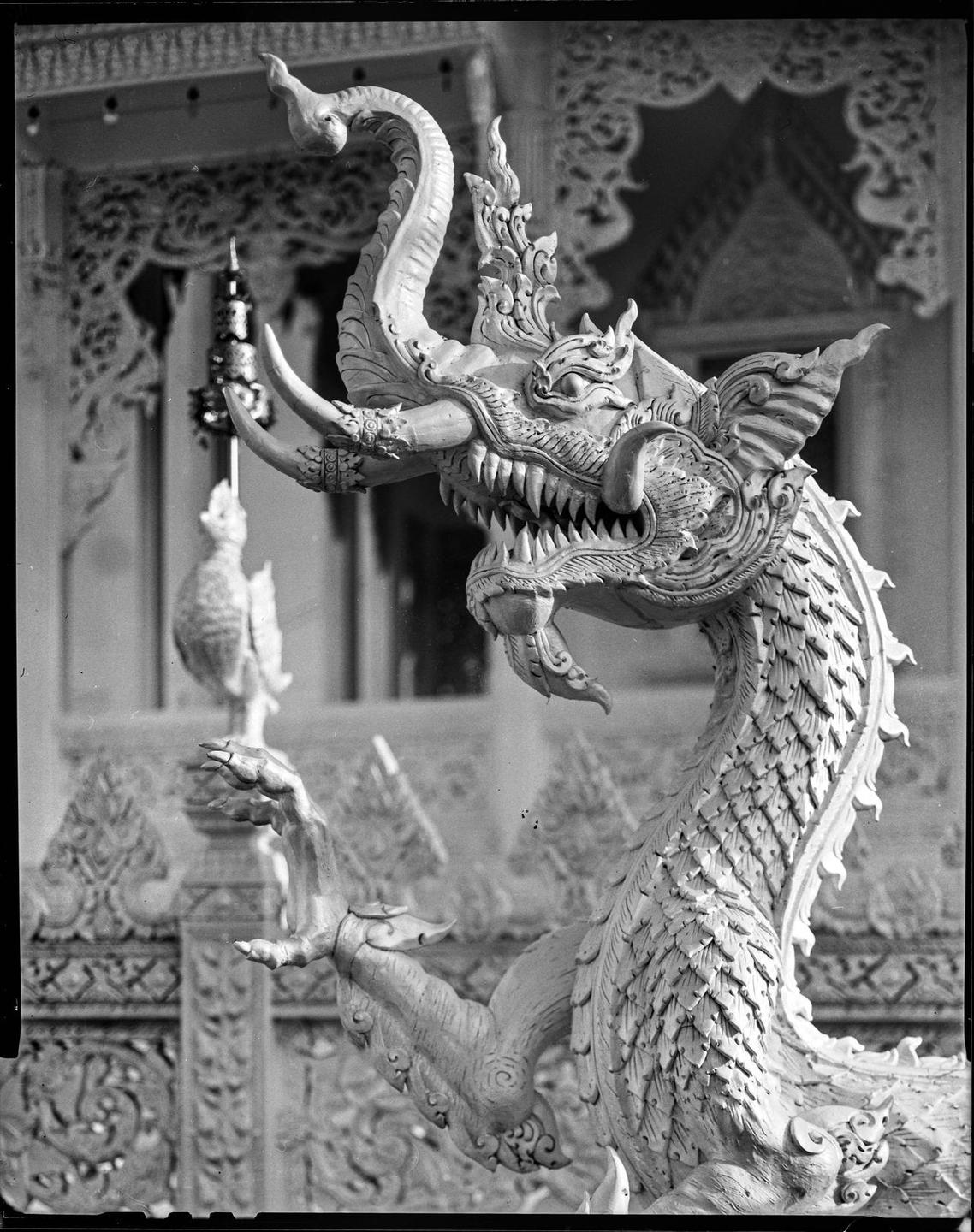 A detailed statue of a mythical creature with tusks and scales is shown in black and white.