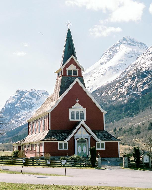 A red church with a tall steeple stands in front of snow-capped mountains.