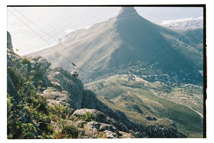 A cable car descends a mountain with a city and ocean in the background.