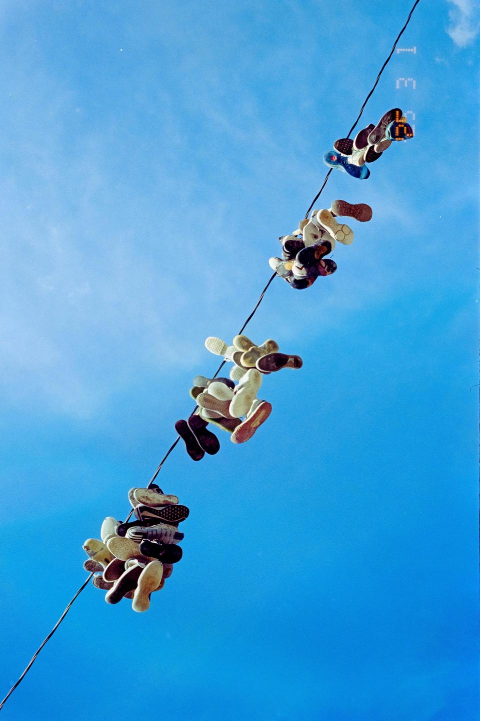 Many pairs of shoes hang from a wire against a bright blue sky.