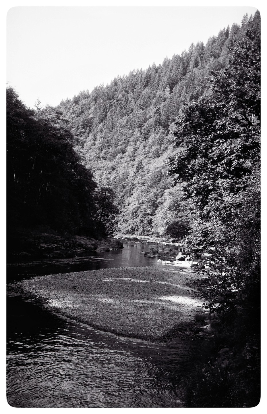 A river flows through a valley with forested hillsides under morning light.