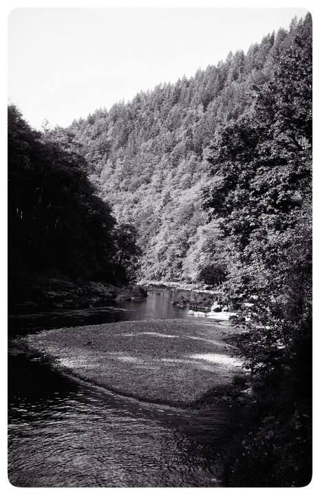 A river flows through a valley with forested hillsides under morning light.
