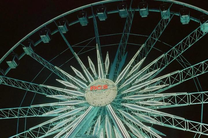 A ferris wheel with illuminated spokes and a central logo is visible against a dark night sky.
