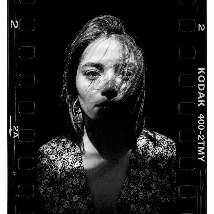 A woman with hair across her face is illuminated by a strong light source from the left, casting a shadow across her face and chest.