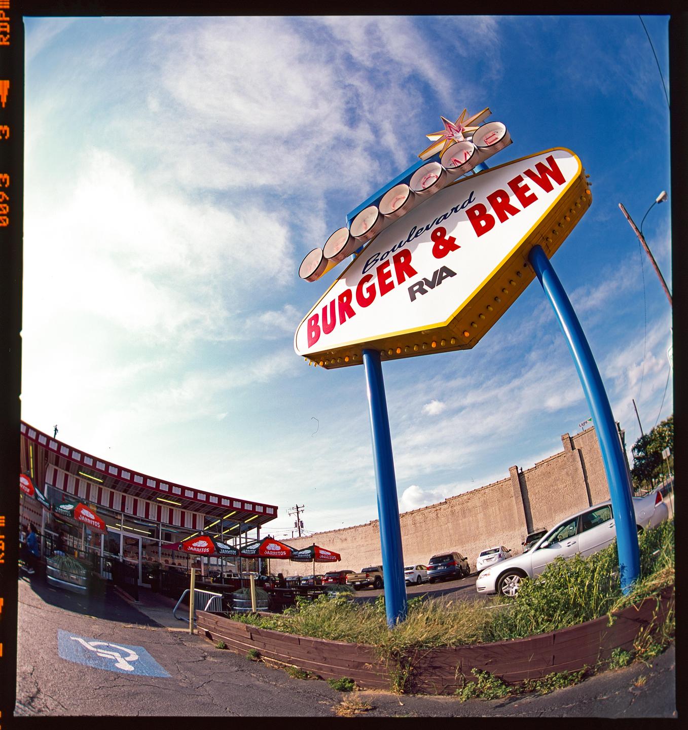 A large sign for "Boulevard Burger & Brew" stands prominently against a bright blue sky with wispy clouds, with a restaurant building and parking lot visible in the background.