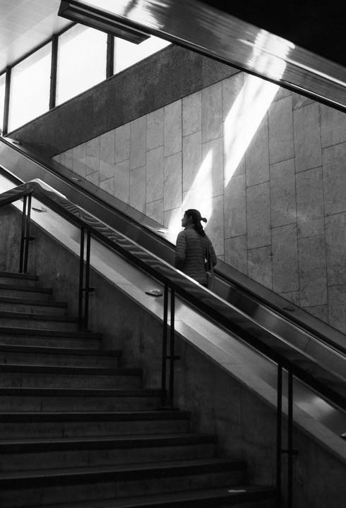 A woman rides an escalator next to a staircase in a building with light shining through a window.