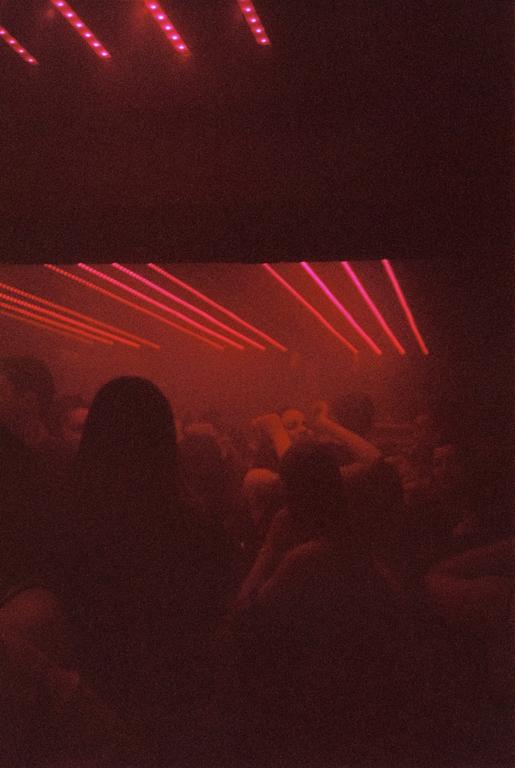 A crowd of people is visible in a dark room illuminated by red laser lights.