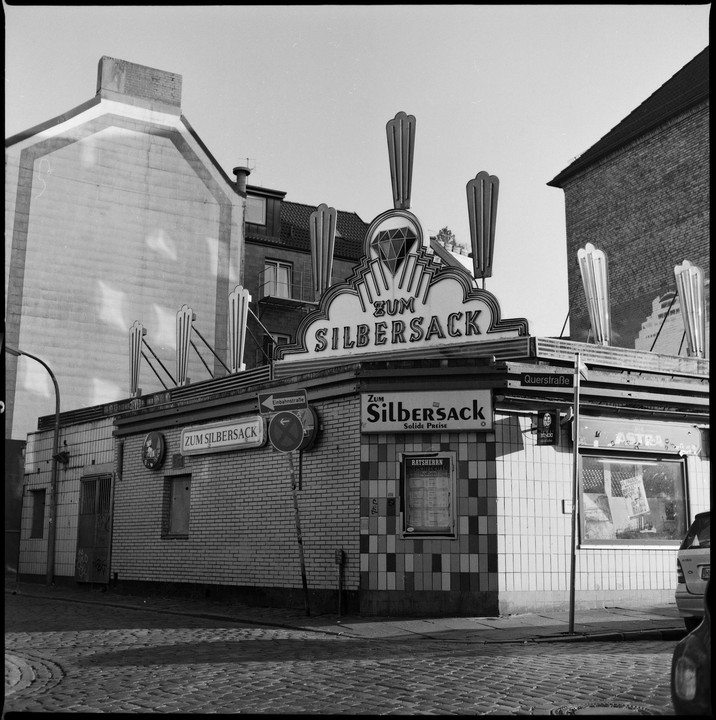 A street corner building with a prominent "Zum Silbersack" sign and decorative elements stands under a clear sky.