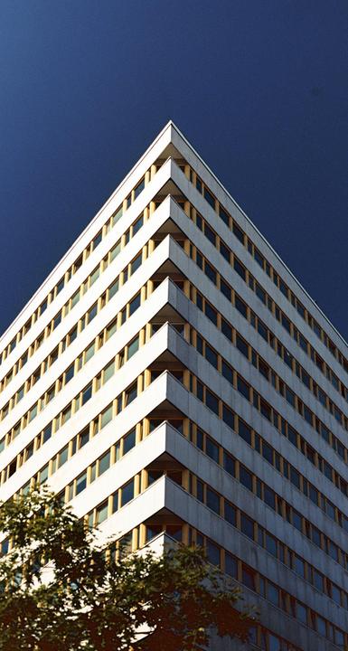 A tall building with many windows is photographed from below against a dark blue sky.