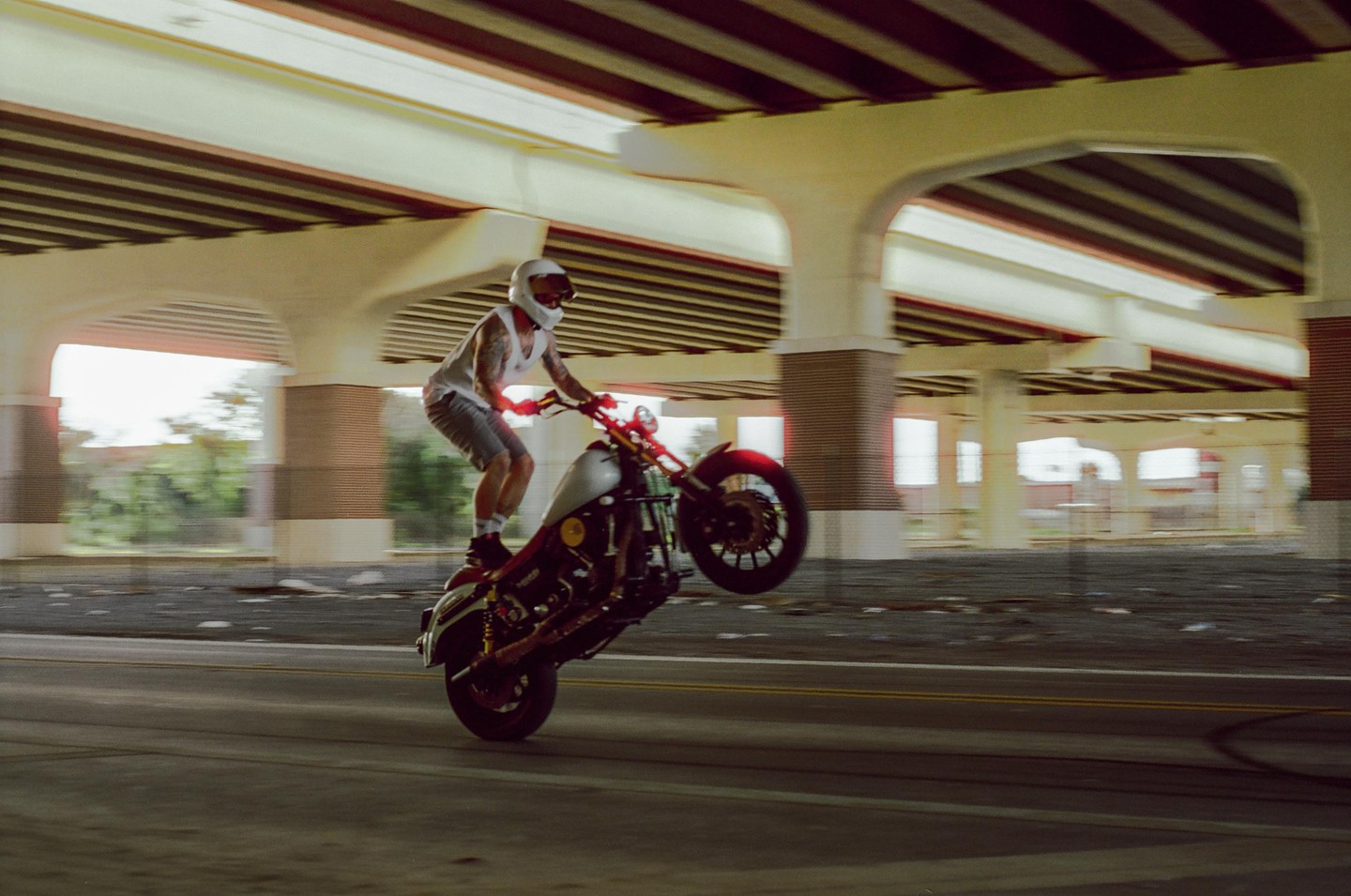 A man on a motorcycle performs a wheelie under a bridge.