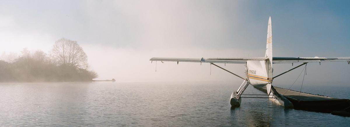 A seaplane is docked on a foggy lake with an island of trees in the distance.