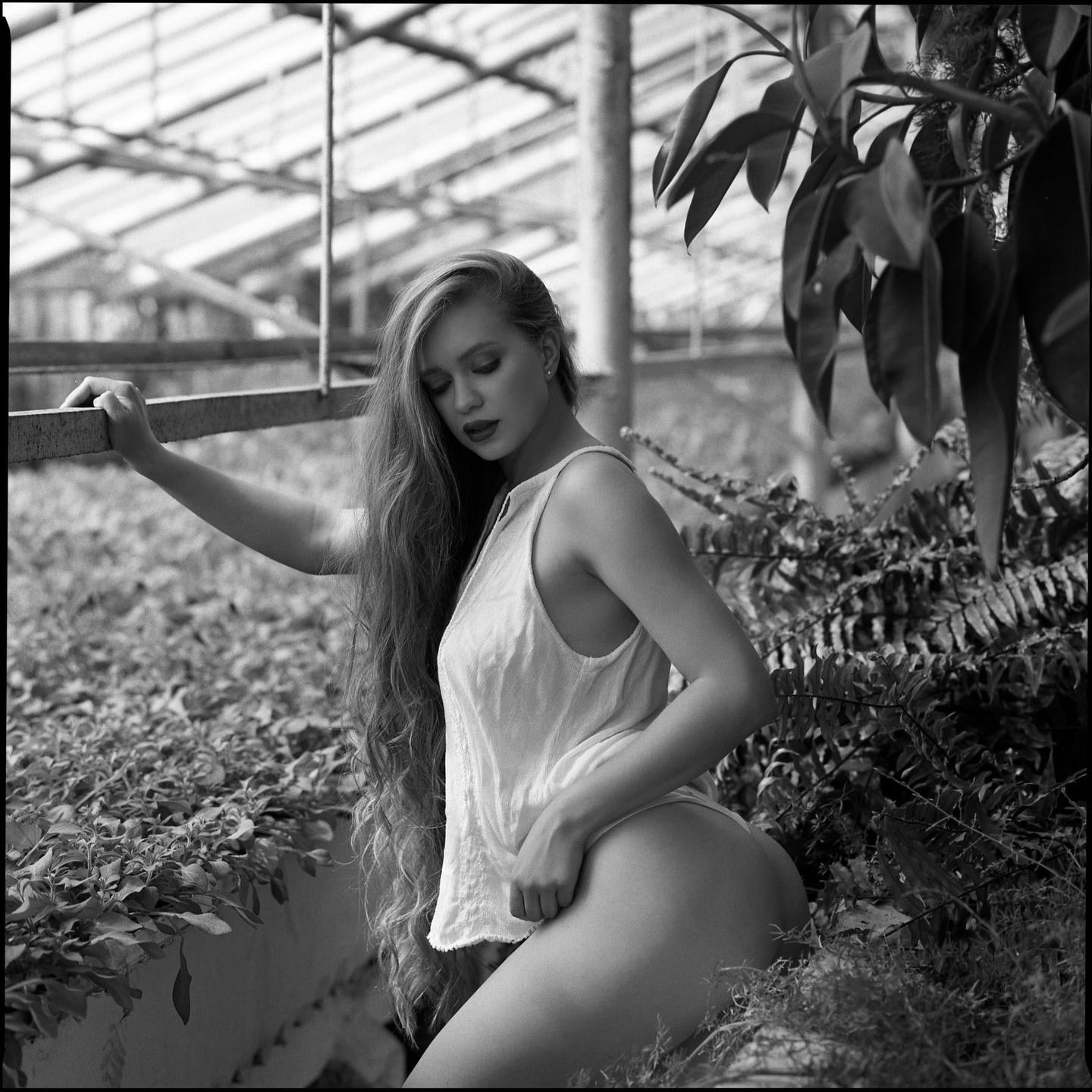 A woman with long hair poses in a greenhouse.