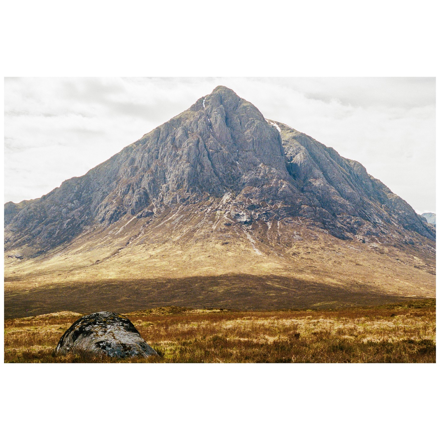 A large mountain rises above a field with a single boulder in the foreground.