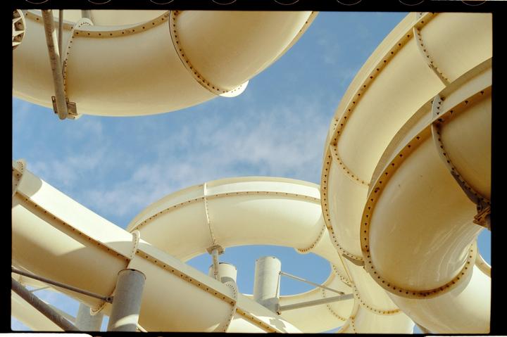 Several white water slides curve against a blue sky with scattered clouds.