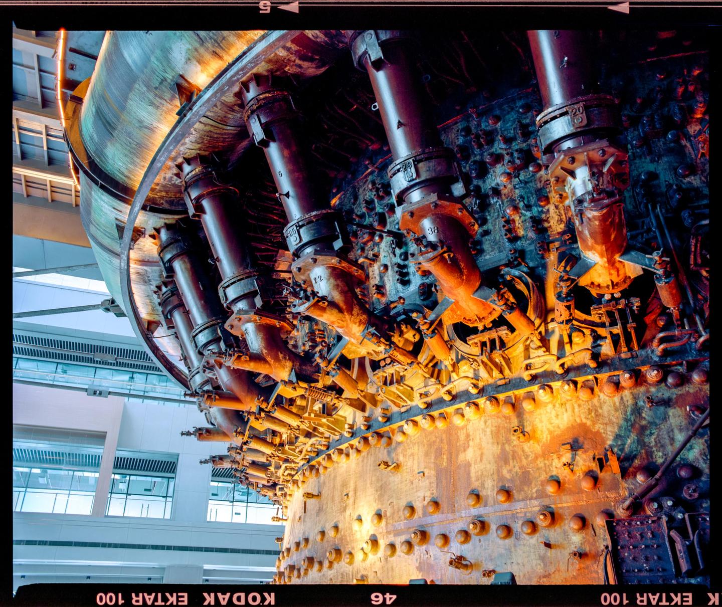 A large, rusty industrial machine with many pipes and bolts is illuminated by warm light.