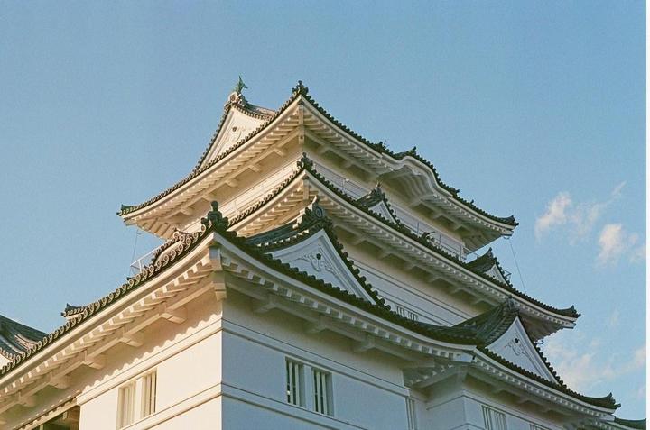 A multi-tiered Japanese castle with intricate roof details stands against a clear blue sky.
