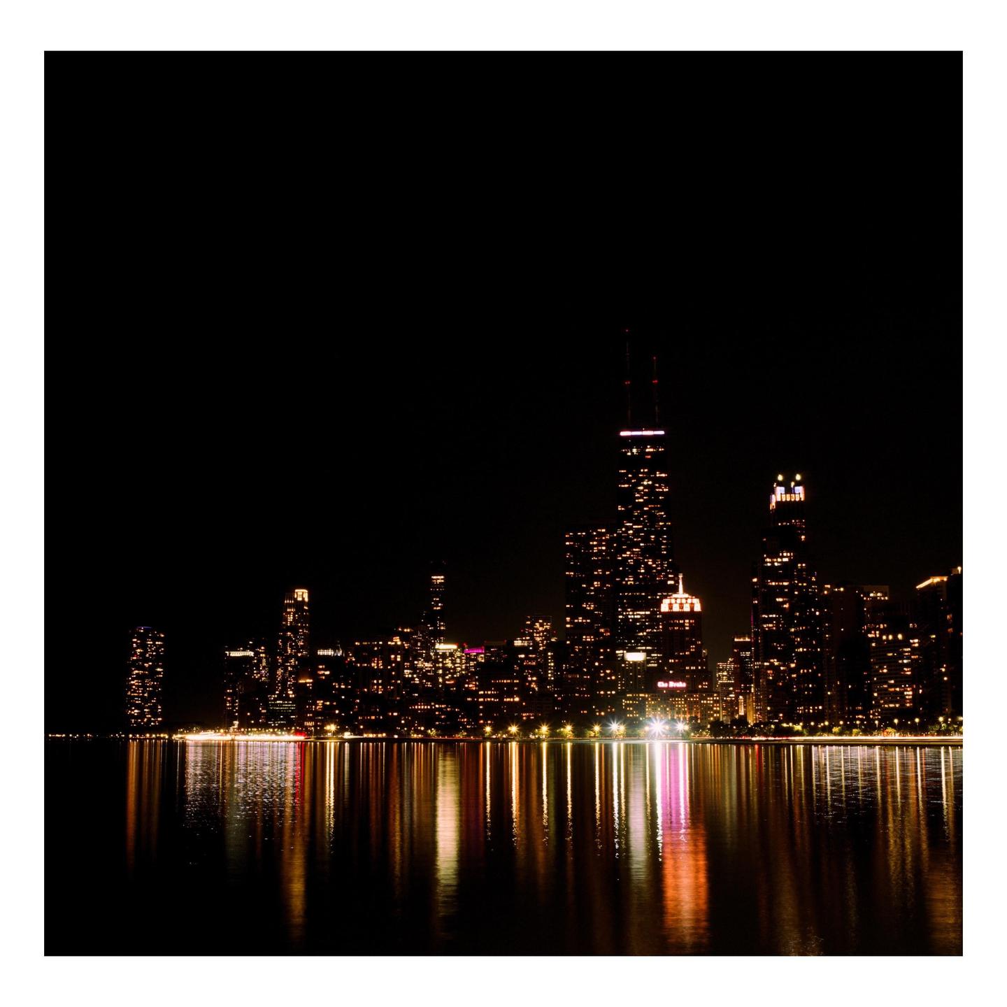A city skyline at night is reflected in the water.