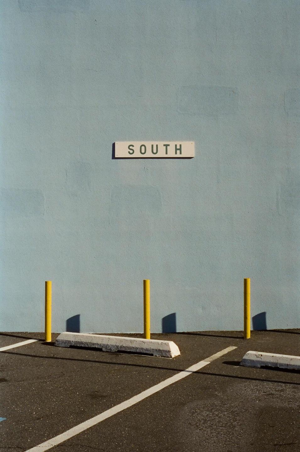 A sign with the word "SOUTH" is mounted on a light blue wall above a parking lot with yellow poles and white parking lines.