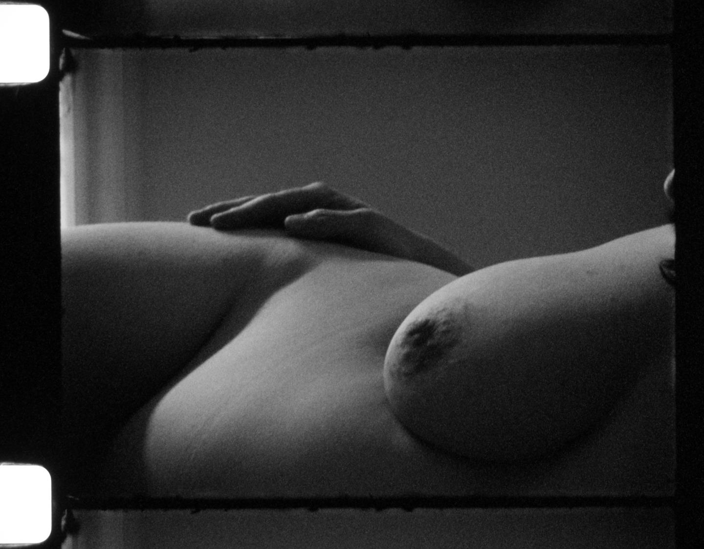 A woman's torso is visible with one hand resting on her stomach and a breast in the foreground.