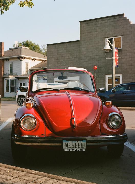 A red convertible Volkswagen Beetle is parked on a street in front of buildings.