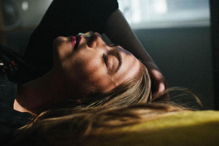 A woman with closed eyes and long hair is illuminated by a shaft of light.