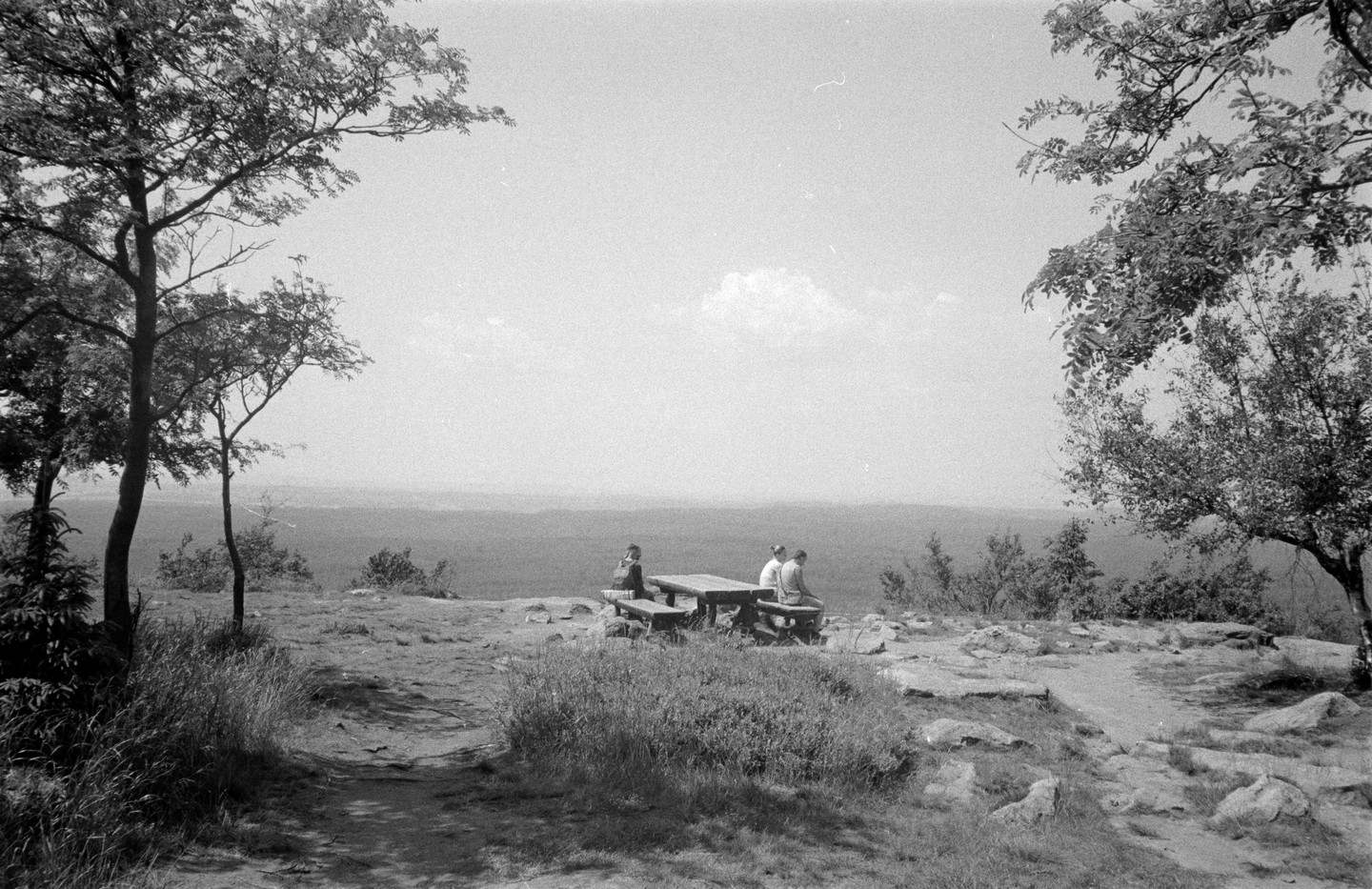 Three people sit at a picnic table on a rocky overlook with a vast landscape stretching into the distance.