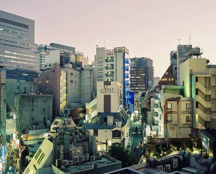 A high-angle view shows a dense urban landscape of buildings and a narrow street at dusk.