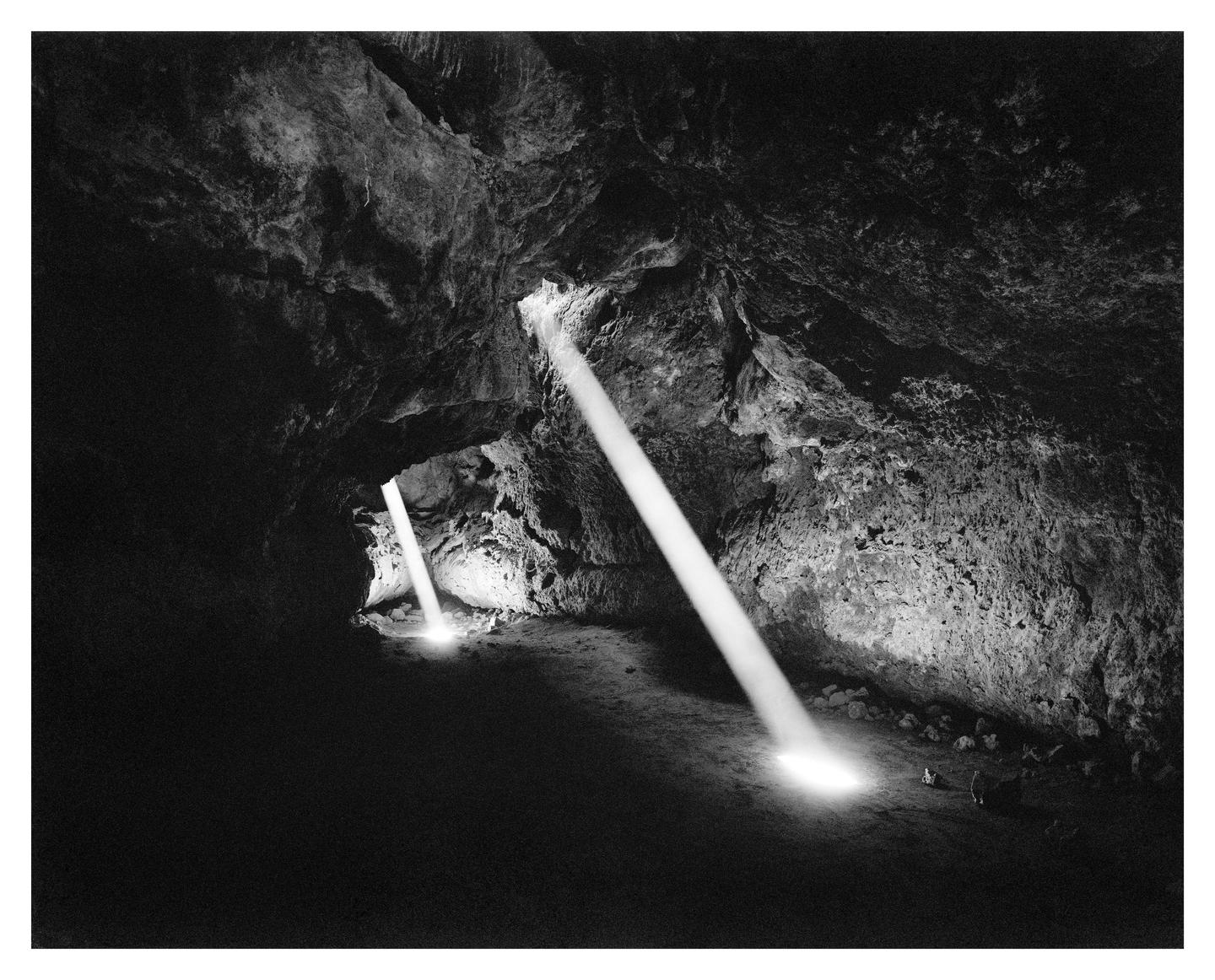 Two beams of light illuminate the dark interior of a cave.