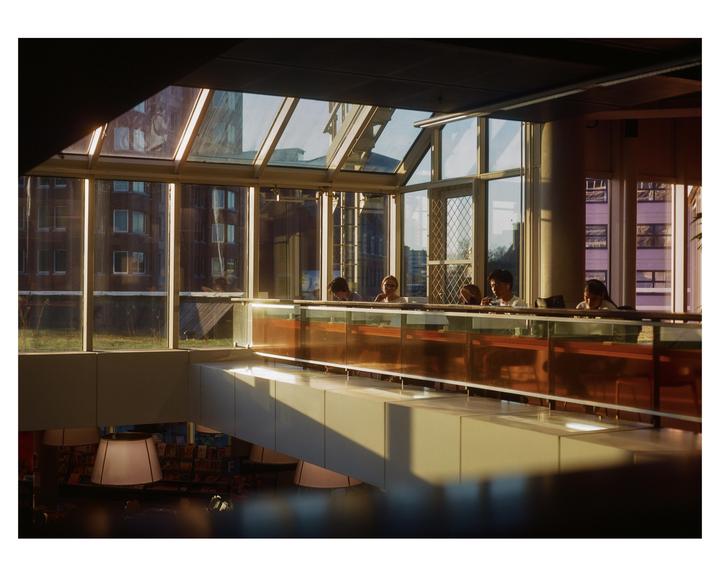 A group of people are seated at a long table in a modern building with large windows and a glass ceiling.
