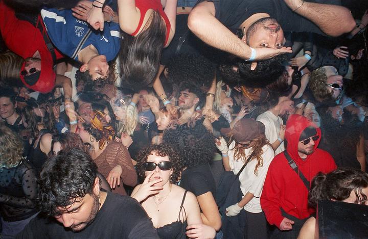 A crowd of people are dancing in a dark club, with some faces appearing upside down.