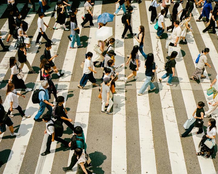 A large group of people are crossing a street on a crosswalk, with some carrying umbrellas.