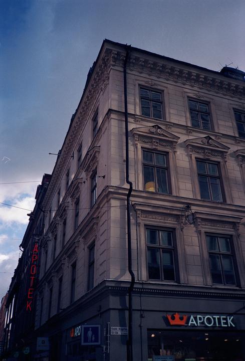A tall building with ornate windows and a neon sign for a pharmacy is seen from a low angle.
