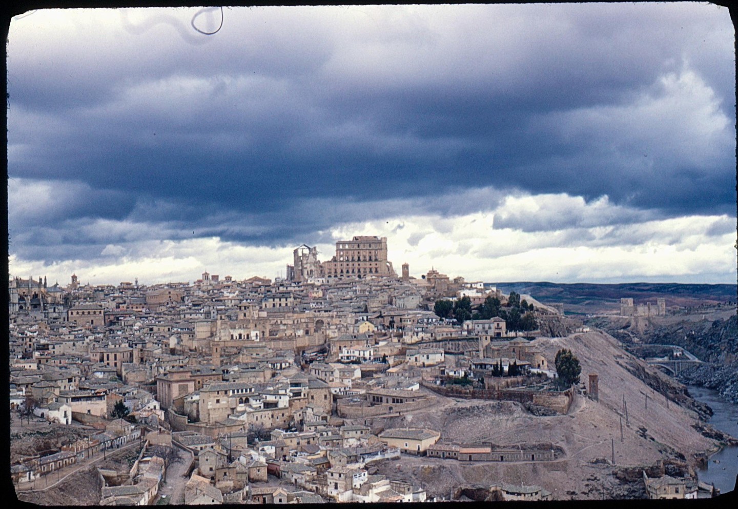 A city with many buildings on a hill is visible under a cloudy sky.