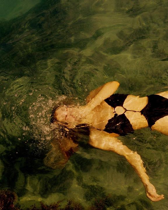 A woman in a black and white swimsuit floats in green water with her face partially submerged.