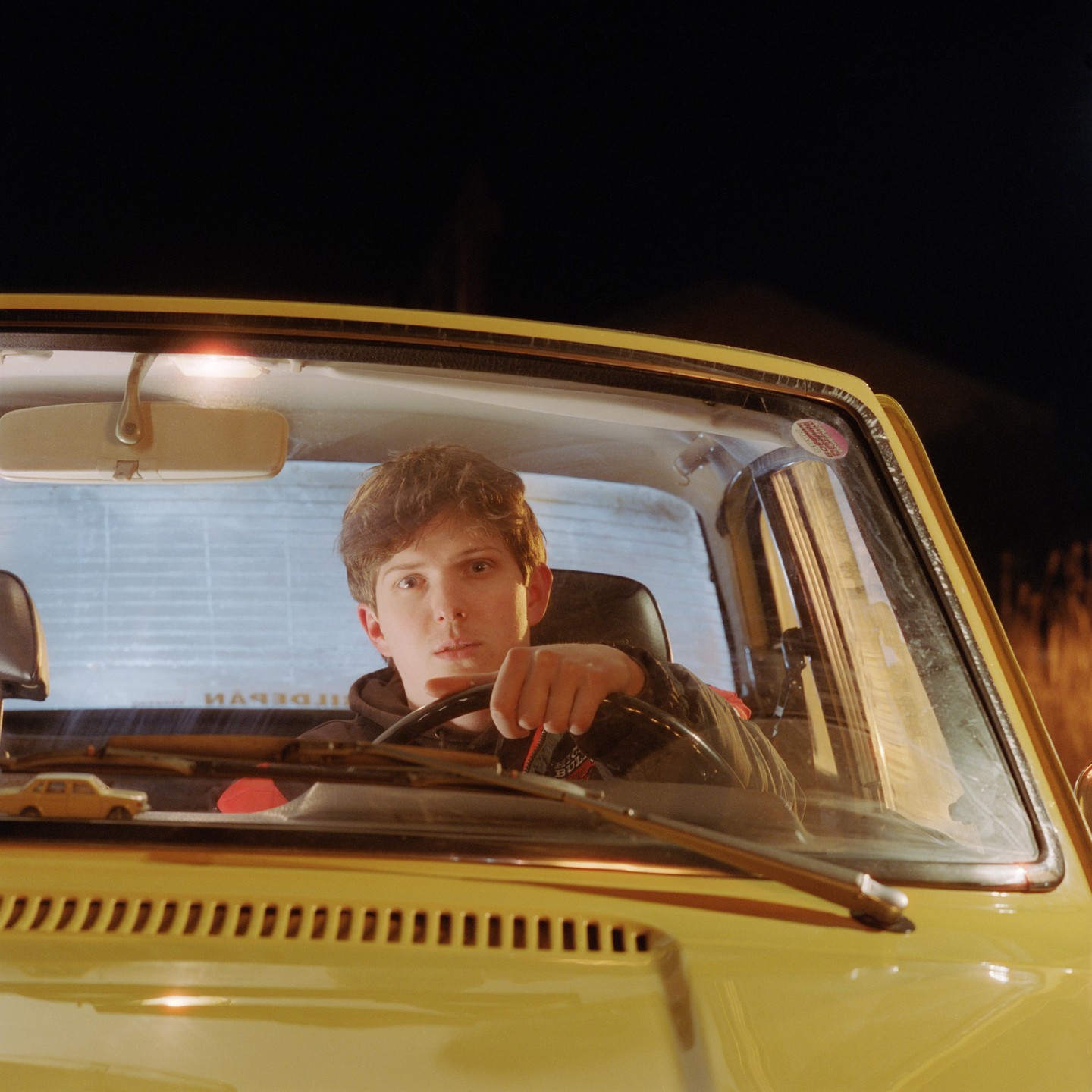 A young man sits in the driver's seat of a yellow vehicle at night.