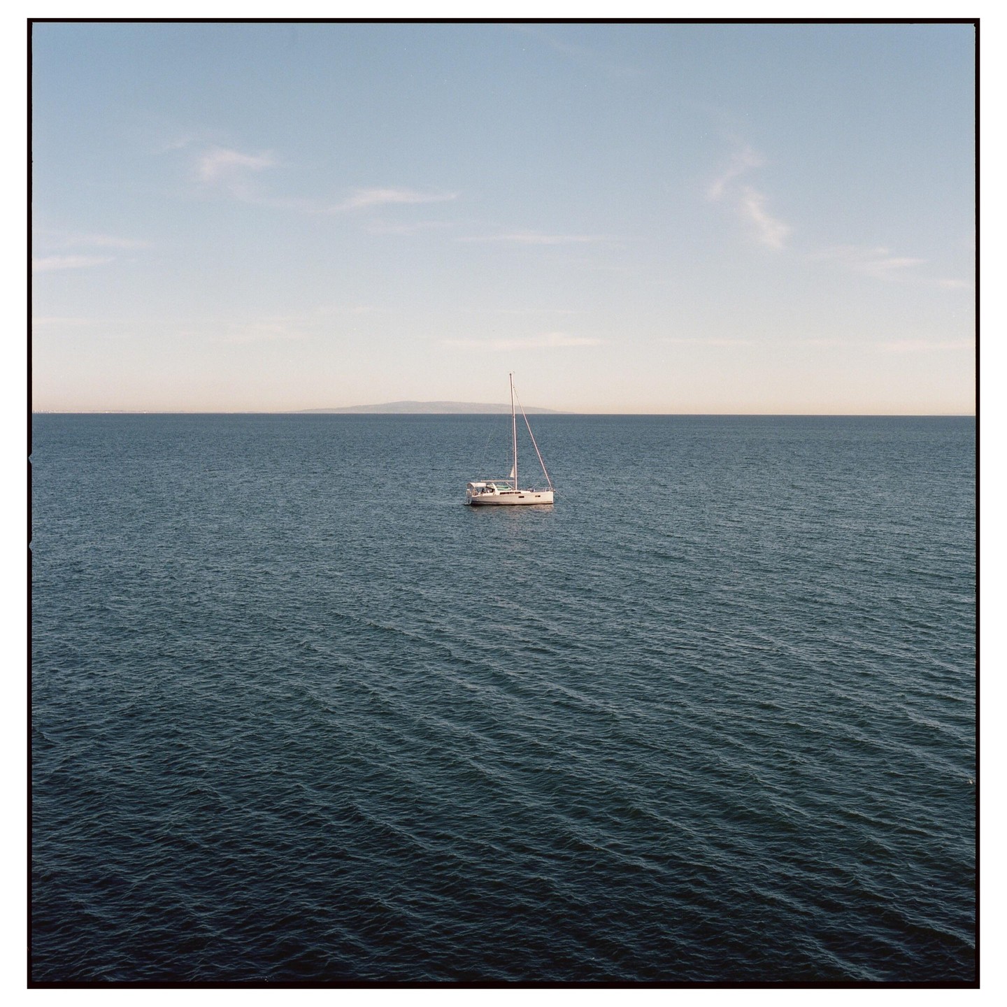 A sailboat floats on the ocean with a distant landmass under a clear sky.