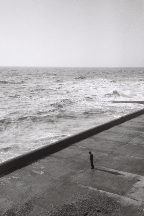 A man stands on a concrete pier looking out at the ocean.