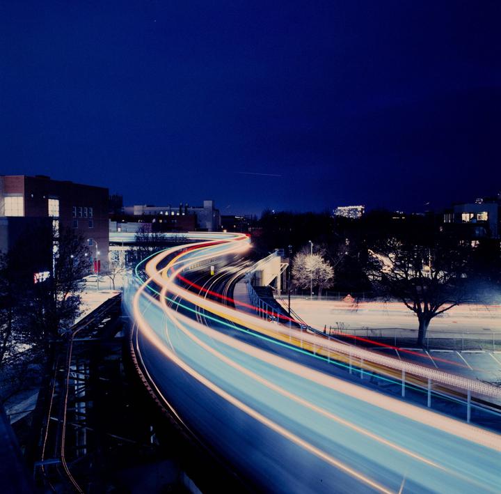Light trails from a moving train curve through a city at night.