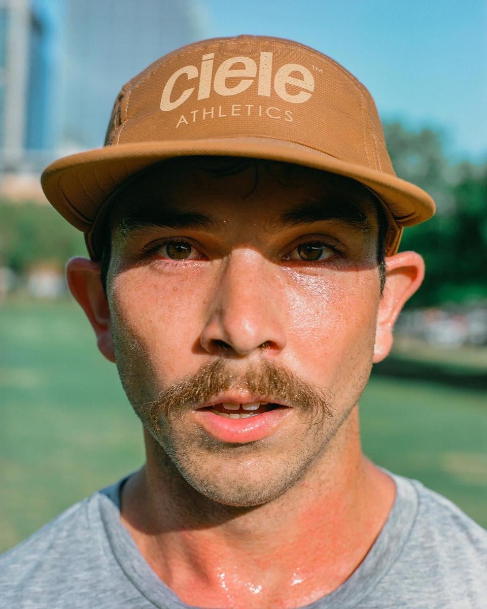 A man with a mustache and a brown cap is sweating after a run.