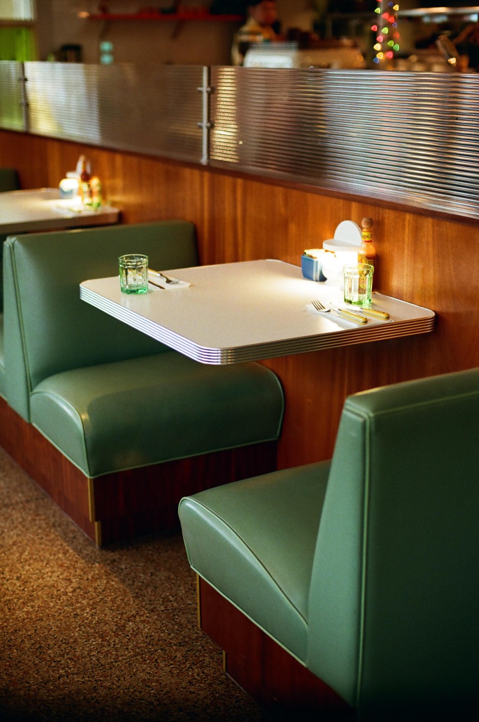A diner booth with green upholstery and a white table is set with a glass and cutlery.