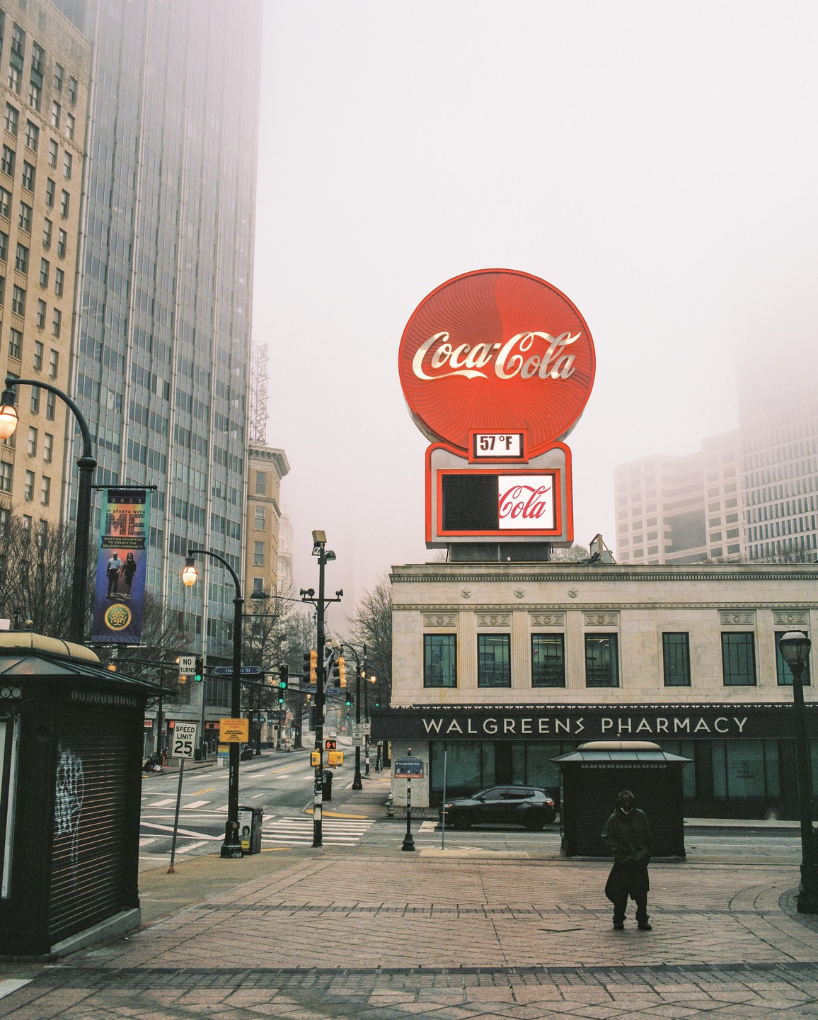 A person stands on a city street with a large Coca-Cola sign and a Walgreens pharmacy in the background.